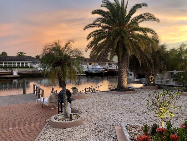 A waterfront property with a dock, palm trees, and a boat docked in the background.