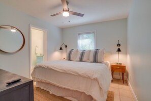 A bedroom with a bed, bedside lamps, a ceiling fan, a mirror, and a window.