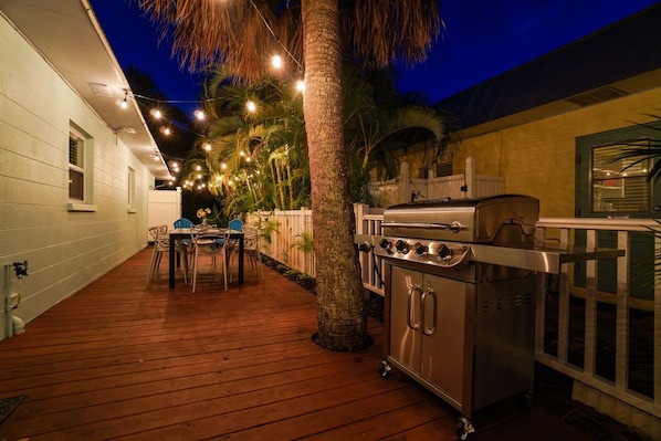 En udendørs patio med grill, træterrasse, stole og lyskæder.