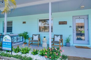 A light blue building with a sign reading 'Rum Dog' and a number '205'. There are wicker chairs and potted plants on the porch.