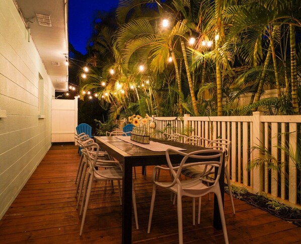 An outdoor patio with a wooden deck, white railing, and string lights.