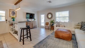 A spacious living room with a white sofa, a coffee table, and a kitchen area with a bar.