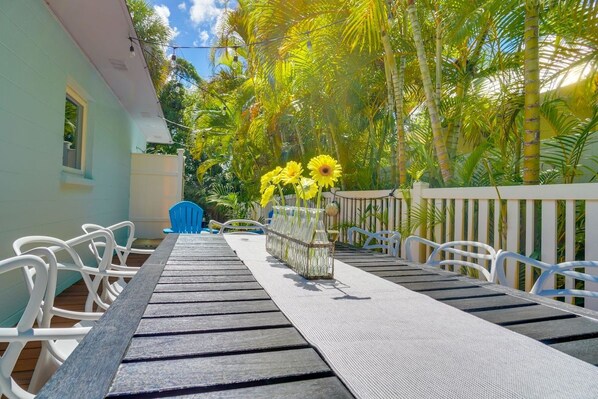 An outdoor dining area with a long table, chairs, and a vase of yellow flowers.