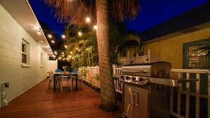 An outdoor patio with a grill, wooden deck, and string lights.