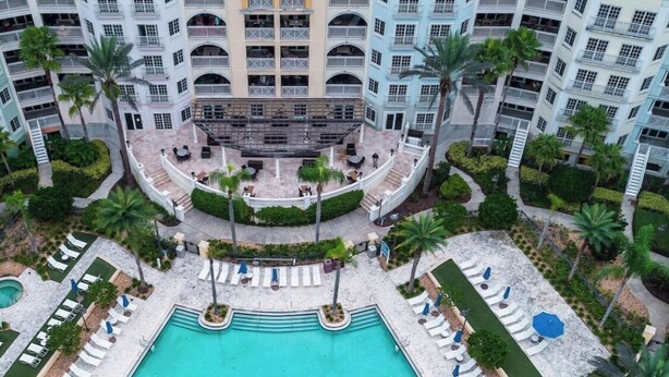 Un hôtel à plusieurs étages doté d’une piscine centrale, entourée d’espaces de détente et de palmiers.