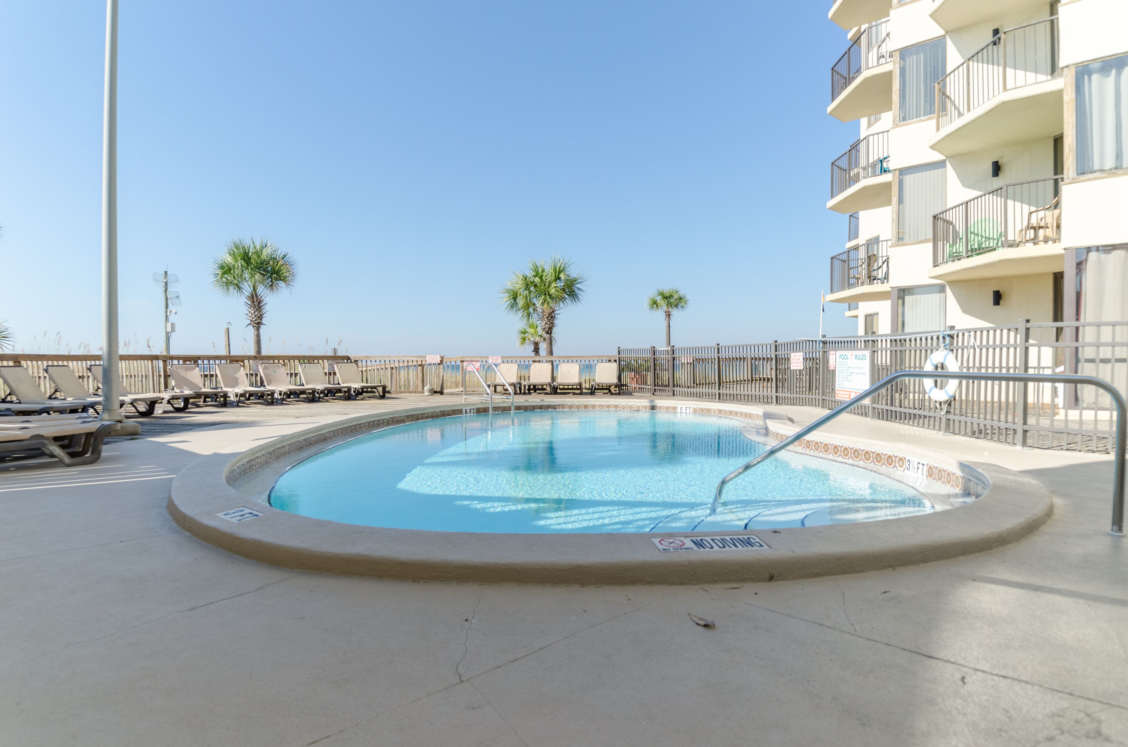 Une piscine avec des chaises longues et un bâtiment doté de balcons.