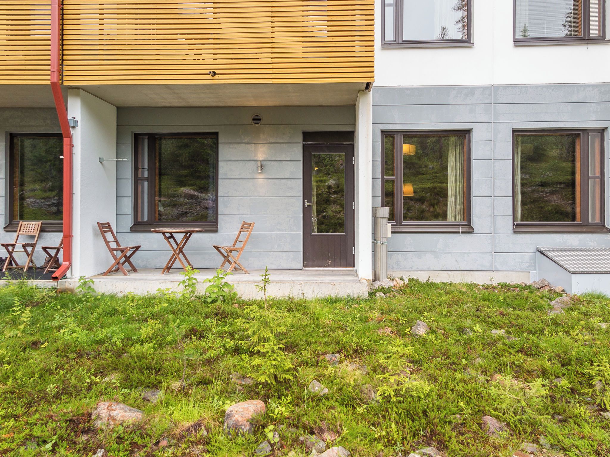 A modern two-story building with a covered porch, outdoor seating, and a stone pathway leading to the entrance.