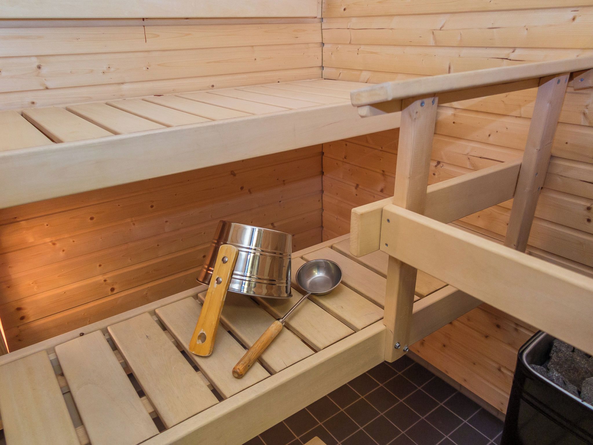 Un sauna avec des bancs en bois et un seau en métal.