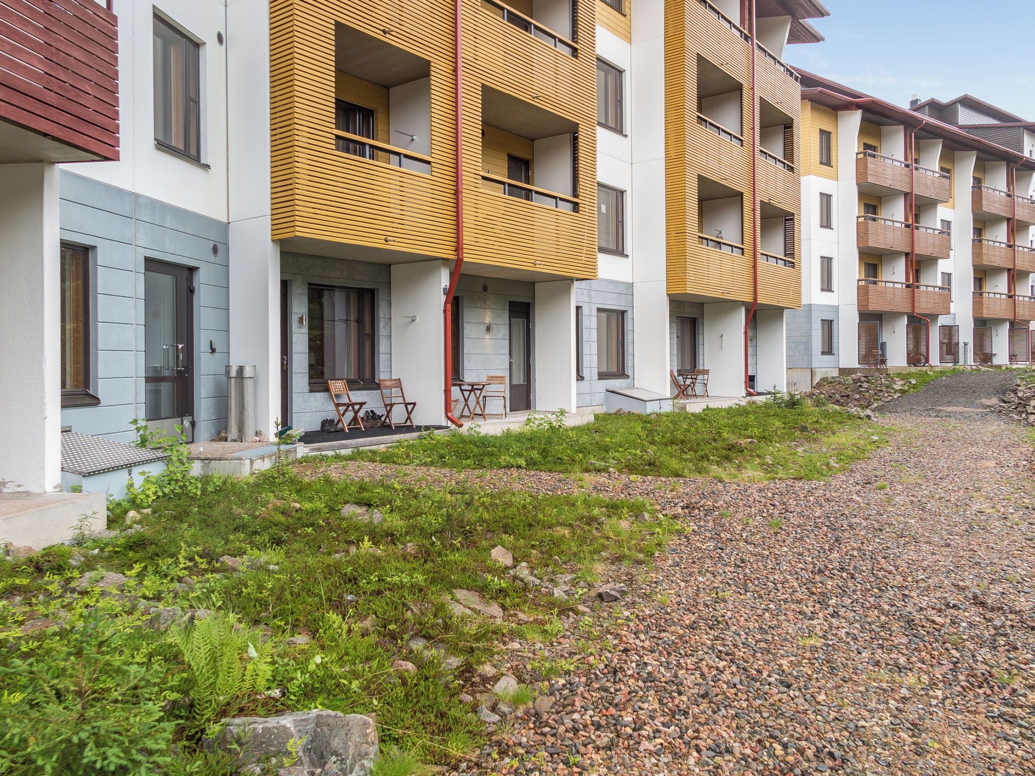 Een modern appartementencomplex met meerdere balkons, een grindpad en terrasmeubels.