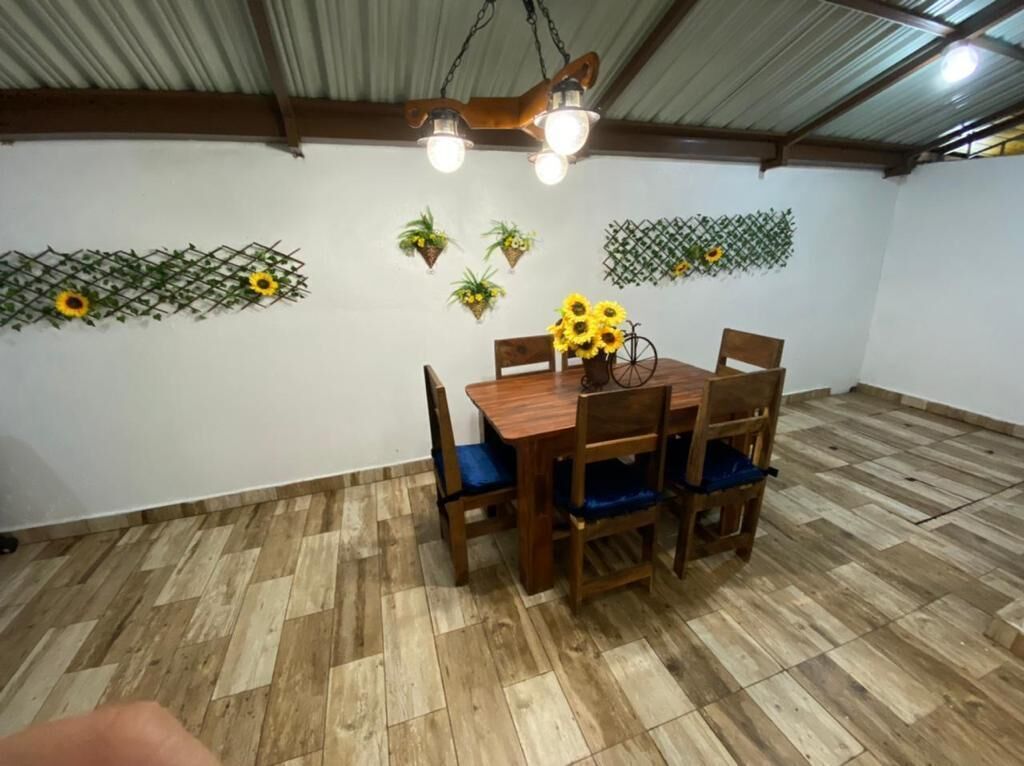 En matplats med ett träbord och stolar, en hängande lampa och väggmonterade blomkrukor med solrosor.