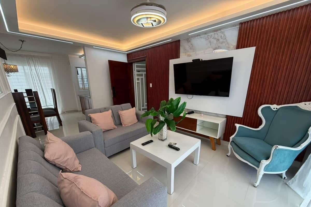 Un salon moderne avec un canapé, un fauteuil, une table basse et un téléviseur fixé au mur.