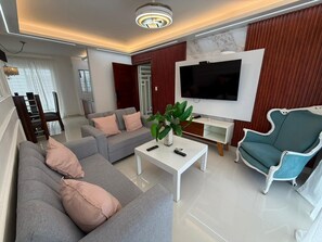 Un salon moderne avec un canapé, un fauteuil, une table basse et un téléviseur fixé au mur.