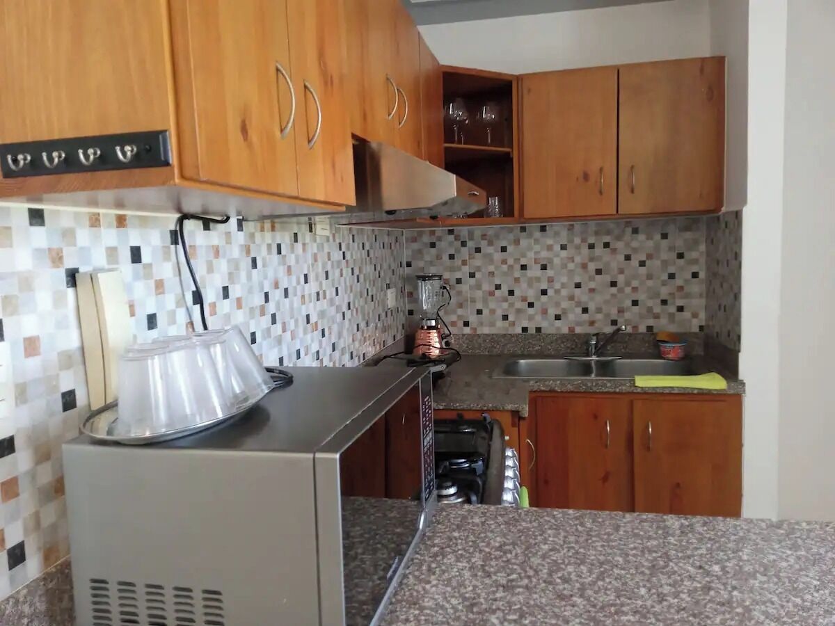 A kitchen with wooden cabinets, a tiled backsplash, and a countertop with a blender and a kettle.