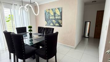 A dining area with a glass table, black chairs, a potted plant, and a wall-mounted painting.