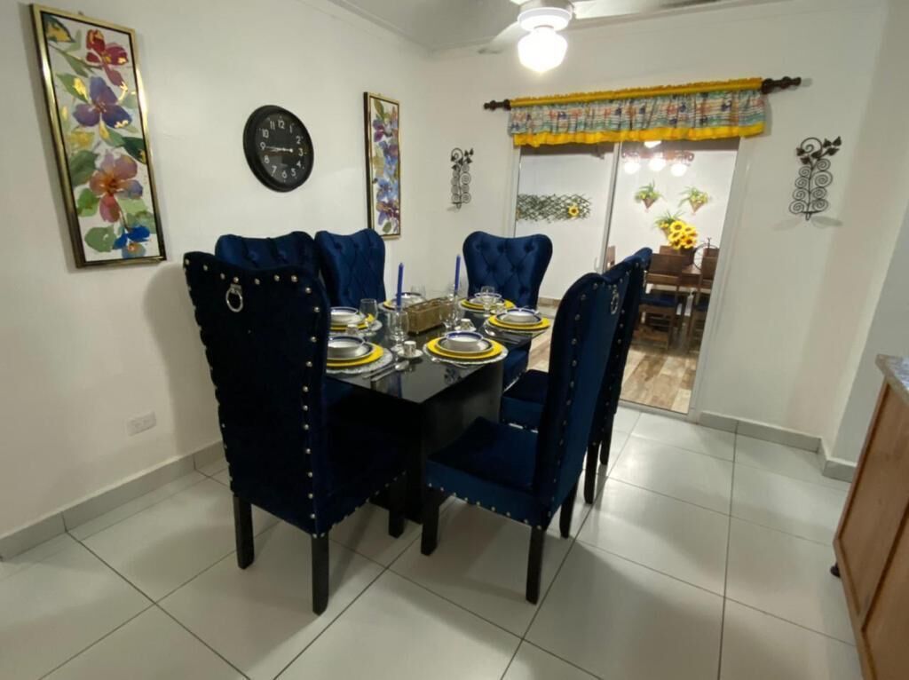 Uma área de refeições com mesa preta, cadeiras estofadas azuis e um jogo de mesa amarelo e preto.