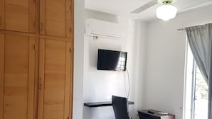Ein Schlafzimmer mit einem Bett, einem Schreibtisch, einem Stuhl, einem Kleiderschrank, einem Deckenventilator und einem an der Wand befestigten Fernseher.