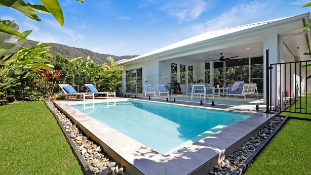 A modern house with a swimming pool, surrounded by lush greenery and a mountain backdrop. - 32c continuously heated pool 300m to beach Seaside@PalmCove (palm cove)