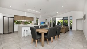 A modern kitchen with a central island, a dining area with a wooden table and chairs, and a living area with a sofa and large windows. - 32c continuously heated pool 300m to beach Seaside@PalmCove (palm cove)
