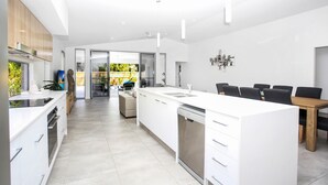 A modern kitchen with a central island, built-in appliances, and a dining area with a wooden table and chairs. - 32c continuously heated pool 300m to beach Seaside@PalmCove (palm cove)