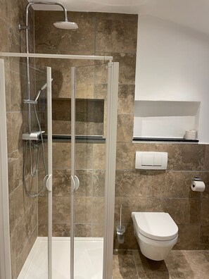 A modern bathroom with a glass-enclosed shower, a toilet, and a shelf with toiletries. - Abendrot Apartment - Ennerla-Hof (Pottenstein)