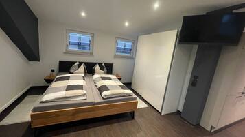 Une chambre moderne avec un grand lit, deux tables de chevet, une armoire et un téléviseur.
