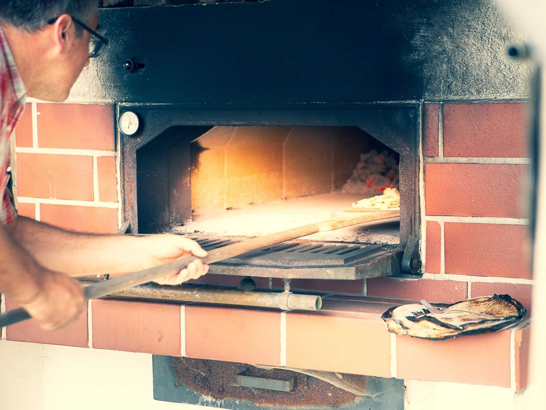 Une personne utilise un ustensile à long manche pour manipuler une pizza à l’intérieur d’un four en briques.