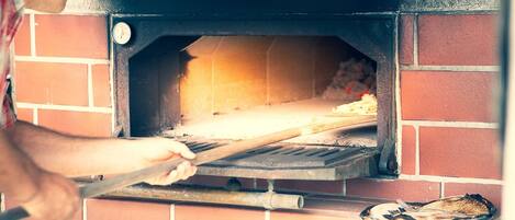 Une personne utilise un ustensile à long manche pour manipuler une pizza à l’intérieur d’un four en briques.
