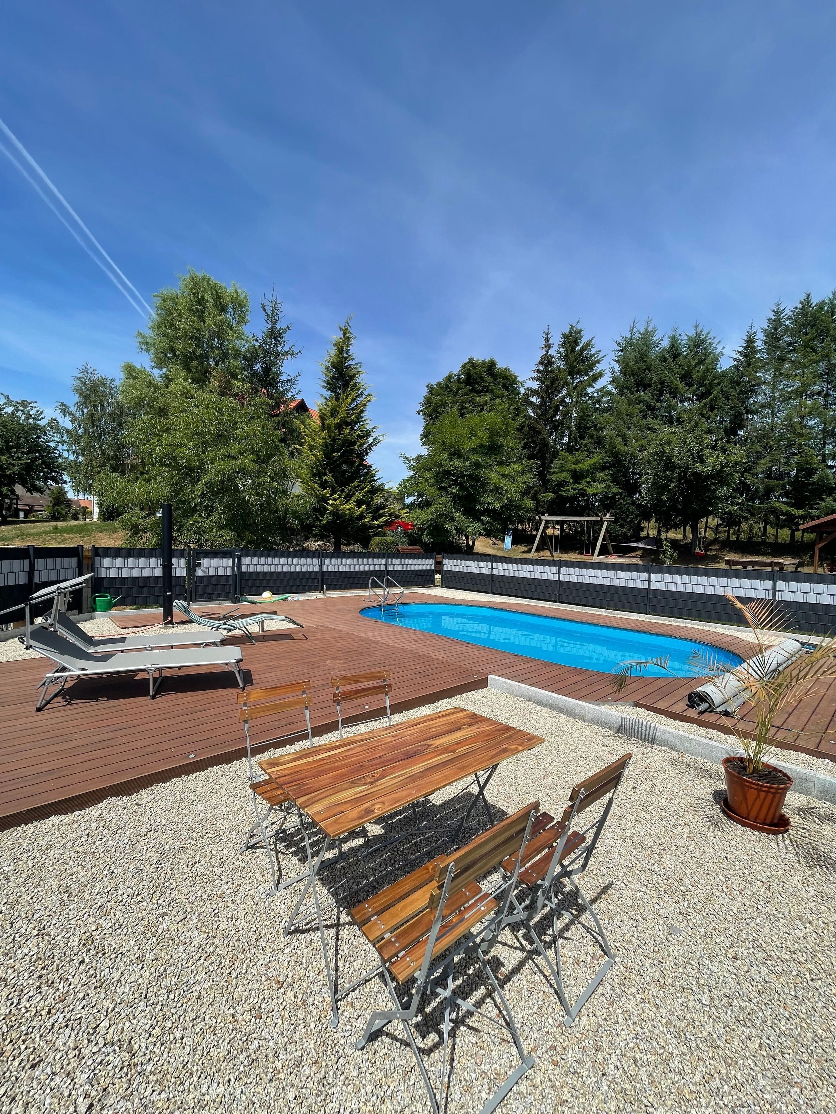 Ein Schwimmbecken mit Holzterrasse, Liegestühlen und einem Tisch.