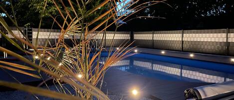 A swimming pool with a tiled deck, surrounded by a low wall and palm plants.