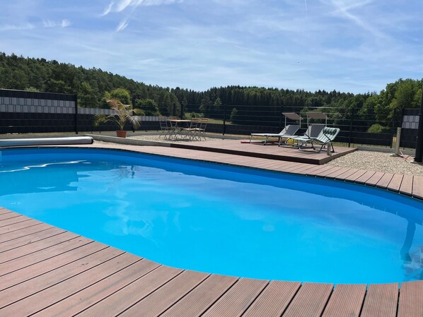 Una piscina con muelle de madera, rodeada por una valla y árboles.
