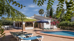 Un área junto a la piscina con sillones de descanso, una mesa con sillas y una piscina pequeña.
