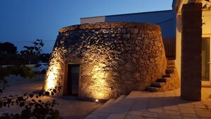 A stone structure with a door, illuminated by warm lighting, and a staircase leading up to it. - trullomio.com - Villa Swimming Pool, BBQ, Trullo, Sea view, WiFi (Torre Suda)