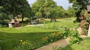 Un jardin agrémenté d’un espace barbecue en briques, d’une balançoire et de diverses variétés de fleurs.