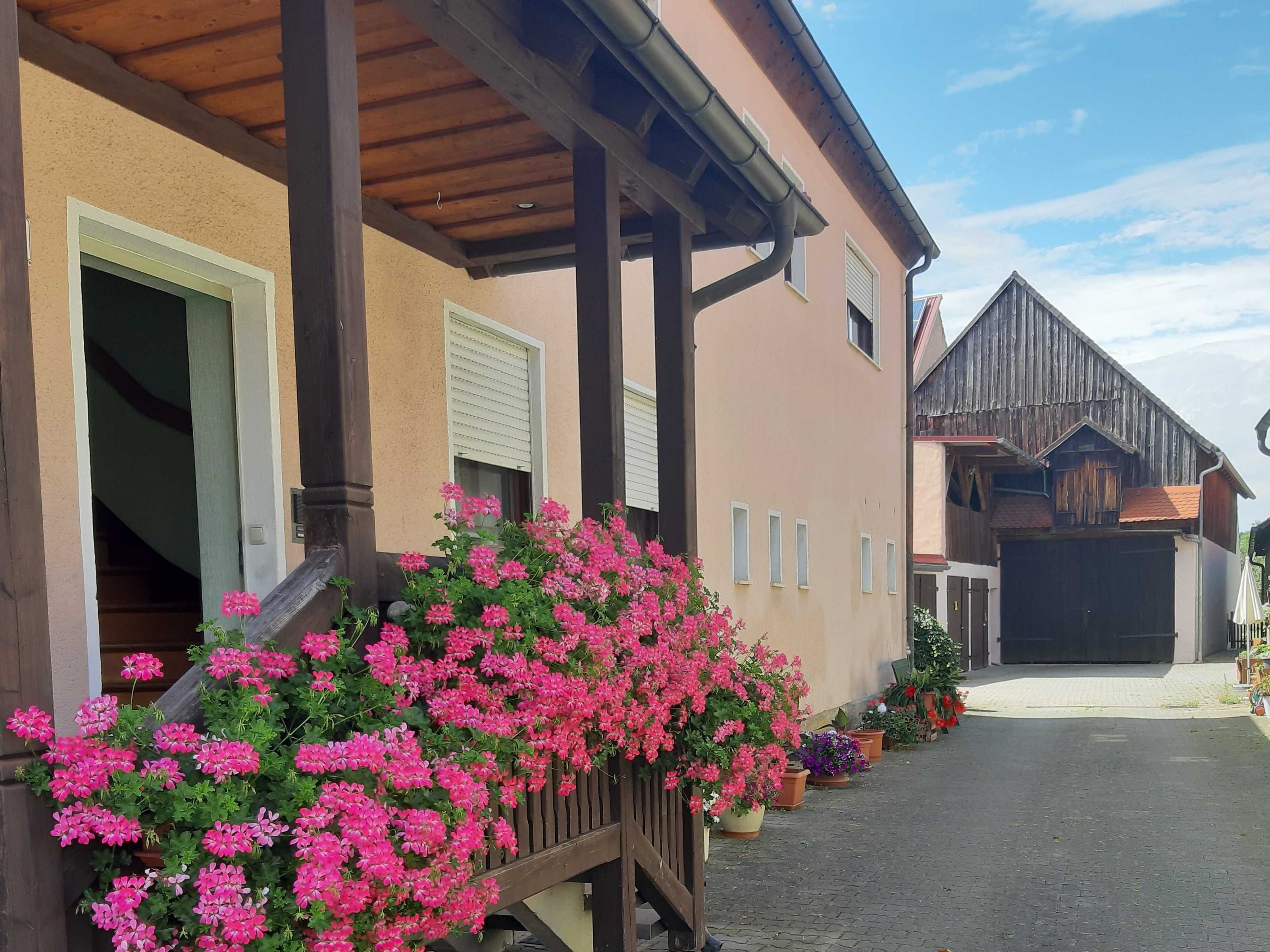 Een gebouw met een overdekte veranda, een garage en een houten omheining met roze bloemen.