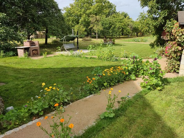 A garden with a brick barbecue area, a swing, and a variety of flowers. - Ferienwohnung Erlwein (Eggolsheim)