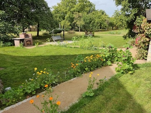 Un jardín con una zona de barbacoa de ladrillo, una hamaca y diversas flores.