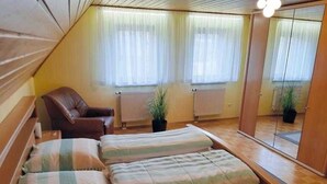Et værelse med skrå vægge, en seng med stribet sengetøj, en stol, to plantekasser og en radiator.