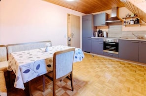 A compact kitchen with a dining area, wooden flooring, and a built-in oven.