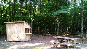 A wooden cabin with a fire pit and picnic table in a wooded area. - Blue Moon - Dark Skies, Spacious, Quiet, Fully Furnished Campsite (Wellsville)