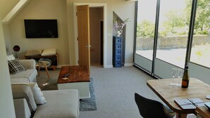 A modern living room with a sofa, a coffee table, a TV mounted on the wall, and a large window offering a view of the outdoors. - Alnmouth Close to Beach and golf with Private Parking and Pet Friendly (Alnwick)
