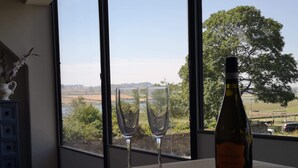 A bottle of wine and two glasses on a table by a window with a view of a park and fields. - Alnmouth Close to Beach and golf with Private Parking and Pet Friendly (Alnwick)
