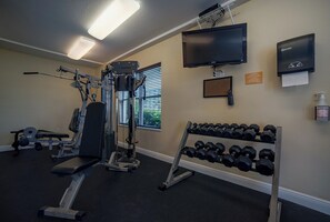 Une salle de sport équipée de matériel d’exercice, d’un téléviseur et d’un distributeur de gel hydroalcoolique de la marque Bay West.