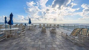 An outdoor terrace with tables and chairs, overlooking a body of water. - #1005 Sanibel - Direct Oceanfront SE Corner Unit (Daytona Beach Shores)
