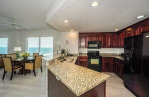 A modern kitchen with granite countertops, dark wood cabinets, a black refrigerator, and a dining area with a table and chairs.