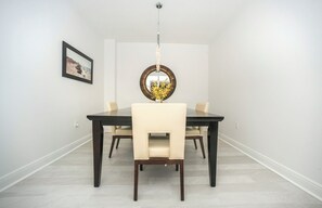A dining area with a dark wooden table, cream-colored chairs, a hanging light fixture, and a framed picture on the wall. - #1005 Sanibel Direct Oceanfront SE Corner Unit 3/3 (Daytona Beach Shores)