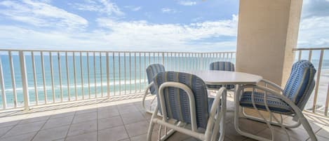 A balcony with a white table and chairs, overlooking a beach with a clear sky.