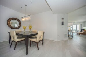 Un coin repas comprenant une table ronde, des chaises, un lustre et un miroir au mur.