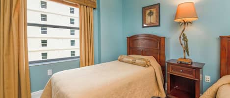 Quarto de hotel com cama, mesa de cabeceira, abajur e janela com cortinas.