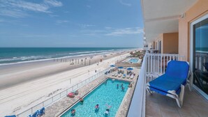 Un balcón con piscina, vista a la playa y sillas de descanso.