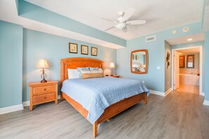 A bedroom with a bed, two nightstands, a ceiling fan, and a bathroom visible through an open door. - Sanibel Condo #302 3/3 Direct Oceanfront NE Corner (Daytona Beach Shores)